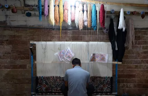 An Iranian man sits in front of a loom to weave a Persian rug