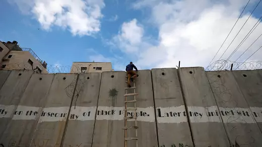 A Palestinian uses a ladder to climb over the wall separating the Israeli and Palestinian sides of the West Bank.