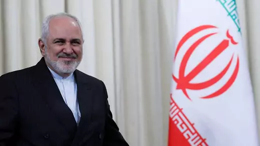 Iran's Foreign Minister Mohammad Javad Zarif standing next to a red, white, green Iranian flag