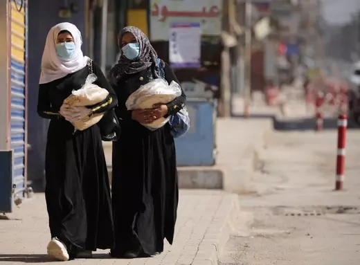 Women hold stacks of bread as they walk along an empty street, as restrictions are imposed as measure to prevent the spread of the coronavirus disease (COVID-19) in Qamishli, Syria.