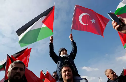 A child sits on a man's shoulders and holds the Turkish and Palestinian flags.