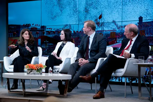 Elizabeth Economy, Mira Rapp-Hooper, Brad Setser, and Richard Haass sit on chairs behind a low white coffee table with orange flowers with a blue backdrop. 