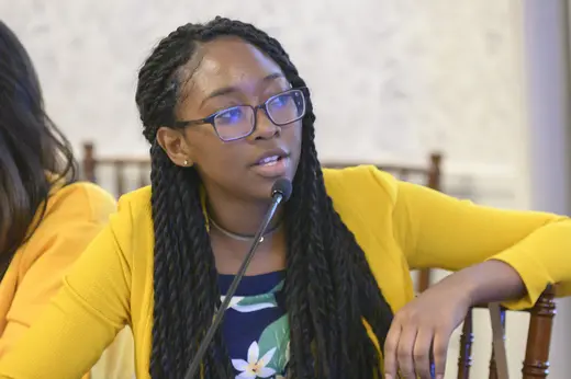 A student wearing floral print and a yellow sweater speaks into a microphone