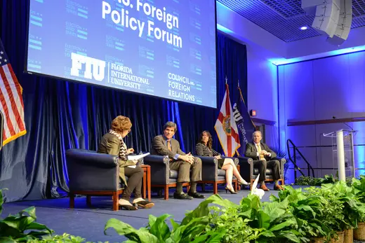 Four panelists sit on stage in front of a blue backdrop and a large screen