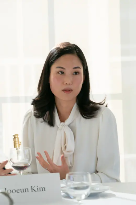 Jooeun Kim, in white, sits at a table in front of a white background