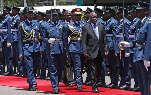 Tanzanian President John Magufuli walks down a red carpet while observing a guard of honor in Nairobi, Kenya. The soldiers are wearing dark blue uniforms; some soldiers are holding swords raised.