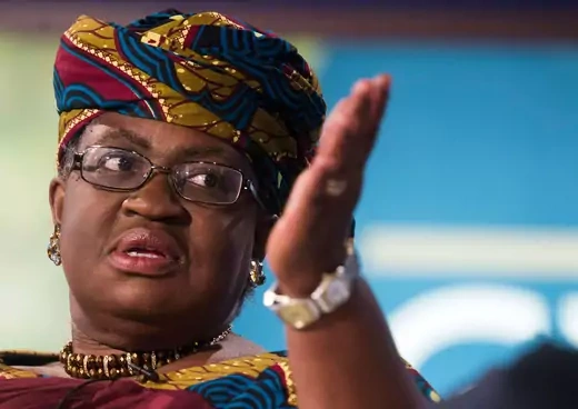 Ngozi Okonjo-Iweala, a Nigerian woman running for WTO director general, raises her left arm while speaking. She is wearing a traditional headdress.