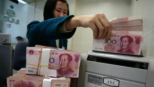 Women holding a stack of Chinese currency at a bank