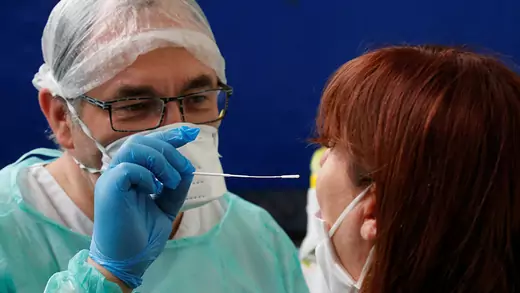 A French doctor, wearing a protective suit and a face mask, administers a nasal swab to a patient at a testing site for coronavirus disease