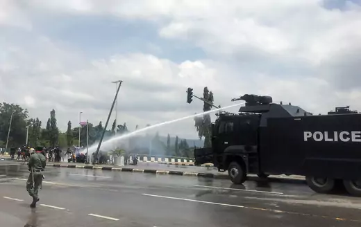 An armored police vehicle shoots a water cannon at protesters in the streets of Abuja, Nigeria.
