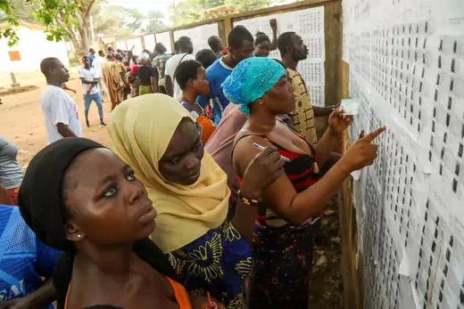 The image shows women in Togo checking their names at a polling location.