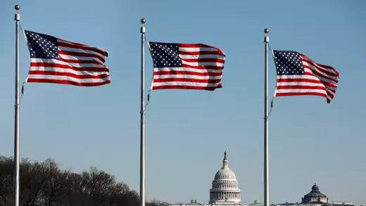 Three U.S. flags in a row with U.S. capitol in the distance
