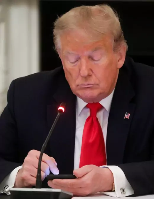U.S. President Donald Trump taps the screen on a mobile phone at the approximate time a tweet was released from his Twitter account.