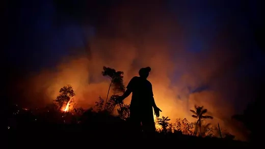 The outline of a man standing in front of a forest fire