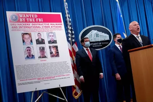 A poster showing six wanted Russian military intelligence officers is displayed.