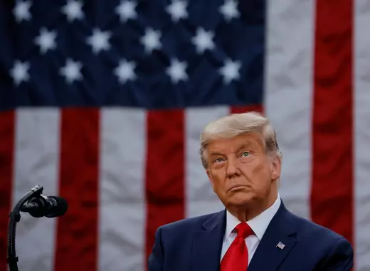 President Donald Trump stands looking up in front of a U.S. flag. 