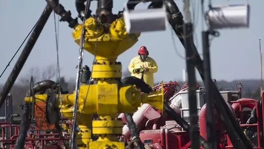 A worker stands behind a well head at a fracturing rig site in Oklahoma.