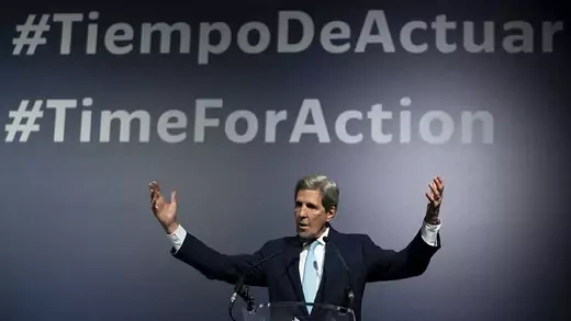John Kerry raises his hands in front of a sign that reads #TimeForAction.