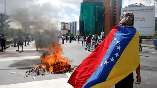 Person wearing a Venezuela at a protest with fire burning in the background