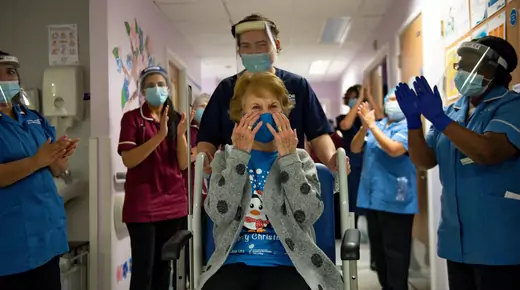 Margaret Kennan is pushed in a wheelchair down a hallway lined with applauding hospital staff. 