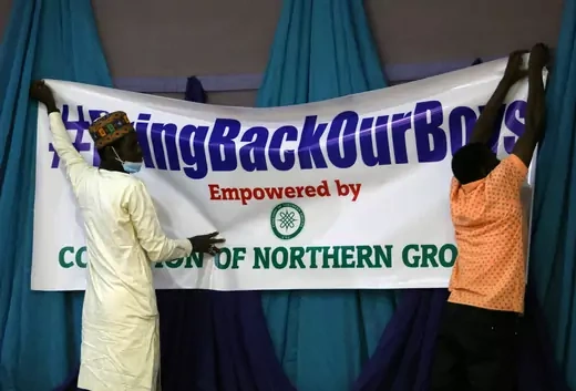 Two Nigerian men, one wearing Islamic dress, put up a sign that readds "#BringBackOurBoys Empowered by Coalition of Northern Groups."