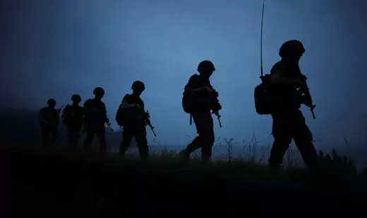 Dark silhouettes of soldiers walking in a line against a dark blue sky