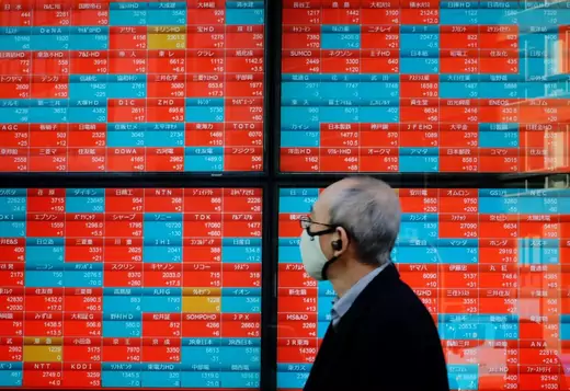 A pedestrian looks at an electronic quotation board displaying companies' stock prices on the Tokyo Stock Exchange in Tokyo on January 13, 2021.
