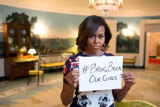 A picture of then-First Lady Michelle Obama standing in the White House, holding a white piece of paper with "#BringBackOurGirls" written in black ink.