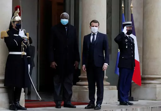 French President Emmanuel Macron and interim Malian President Bah Ndaw are seen outside the Elysee Palace in Paris, both wearing suits and masks. On either side are palace guards, both wearing masks. The guard on the right side of the picture has his hand at salute.