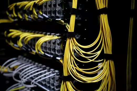 Yellow wires, tied together, hang from the back of a black and gray server.