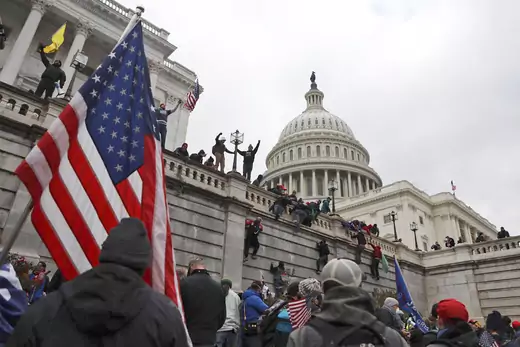 Supporters of U.S. President Donald Trump scale the walls of the U.S. Capitol Building in Washington, D.C. The Capitol building can be seen in the background; an American flag is seen in the foreground.