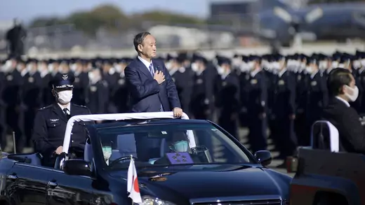 Japanese Prime Minister Yoshihide Suga places his hand over his chest as he rides in a car by defense forces.
