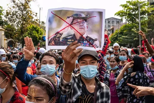 A person in a crowd of protesters holds up an image of Myanmar General Min Aung Hliang with a red x drawn over the general's face.