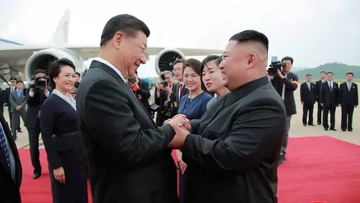 North Korean leader Kim Jong Un holds hands with Chinese President Xi Jinping at the Pyongyang International Airport by a plane and surrounded with people