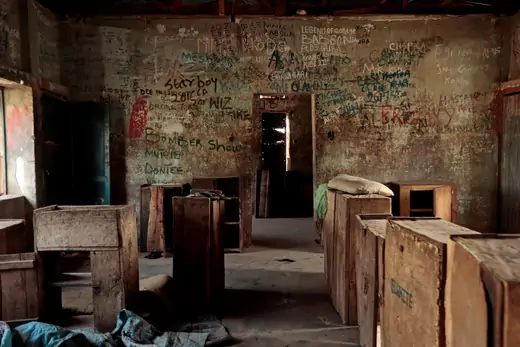 A picture of the interior of an abandoned school in Kagara, Nigeria after gunmen kidnapped dozens of students, relatives, and administrators. Several wooden desks and chairs are seen, while the wall is covered in graffiti.
