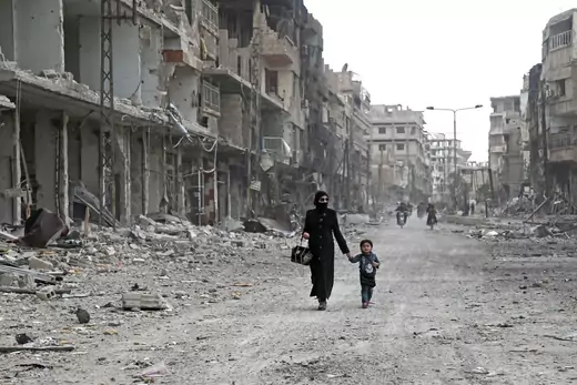 A Syrian woman and child walk down a destroyed street as civilians and rebels prepare to evacuate one of the few remaining rebel-held pockets in Arbin, in Eastern Ghouta, on the outskirts of the Syrian capital Damascus, on March 24, 2018.