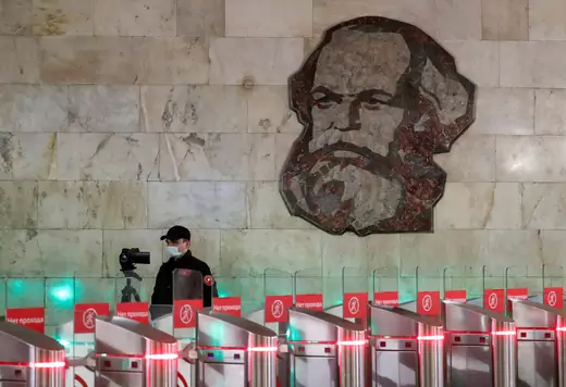 An employee wearing a protective mask uses a device to take passengers' body temperature near a mosaic artwork, which depicts German philosopher Karl Marx, at an entrance to a metro station in central Moscow.