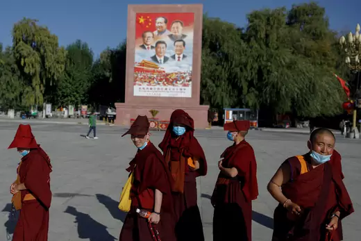 Tibetan Buddhists walk past a poster showing Chinese President Xi Jinping and former Chinese leaders Jiang Zemin, Mao Zedong, Deng Xiaoping, and Hu Jintao during a government-organized tour of Tibet on October 15, 2020.