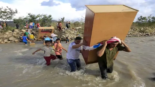 Migrants carrying belongings and crossing a river.