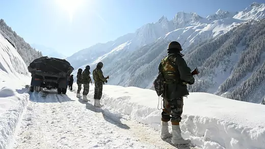 Soldiers stand on a snowy mountain on a sunny day next to a truck. 