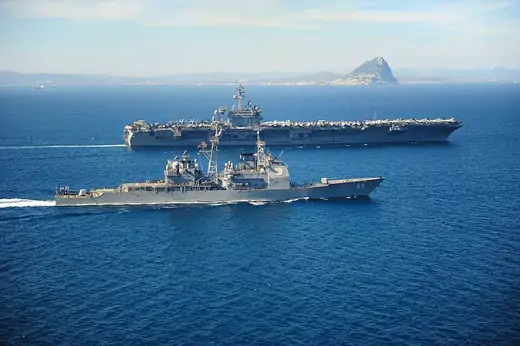 The Ticonderoga-class guided missile cruiser USS Vicksburg (CG 69) escorts the Nimitz-class aircraft carrier USS Theodore Roosevelt (CVN 71) by the Rock of Gibraltar, March 31, 2015, while transiting the Strait of Gibralta.