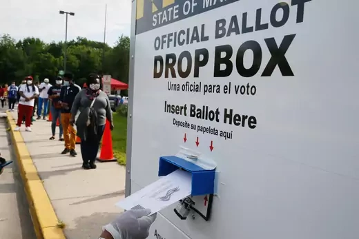 A voter places their ballot in a curbside ballot drop box to help prevent the spread of coronavirus disease (COVID-19) during the Maryland U.S. presidential primary election as other voters stand in a long line waiting to cast their votes in College Park, Maryland.