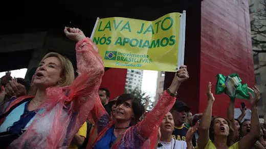 A group of people, several with their arms raised.  One woman is holding a yellow and green sign above her head.