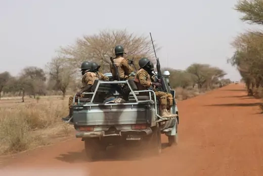 A convoy of Burkinabe sit on a jeep while traveling on a dirt road to patrol.