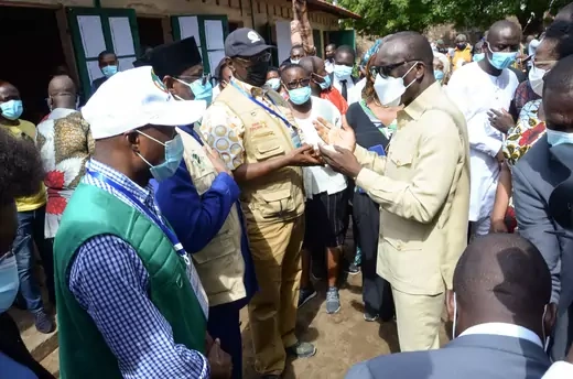Benin President Patrice Talon speaks with a group of observers from the African Union; all are wearing masks, while the observers wear vests and the president wears a suit.