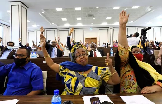 A picture of Somali lawmakers with their hands raised, and one with her left thumb up, as they sit in the lower house of parliament.