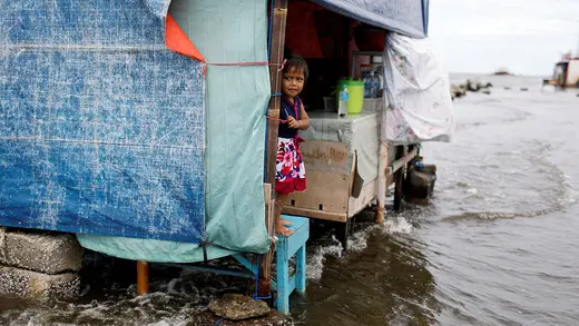 A girl stands on a bench as sea water flows into her home.