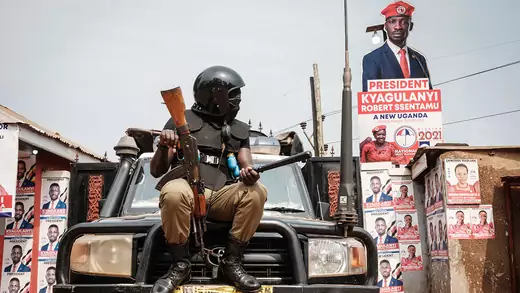 A police officer sits on the hood of a vehicle in front of a gate with posters of opposition figures including Bobi Wine in Kampala, Uganda.