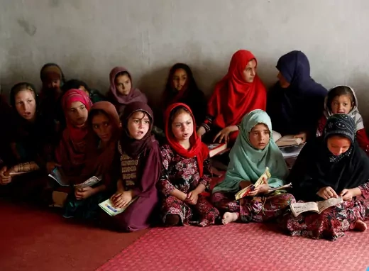 A dozen Afghan girls sitting in a mosque.