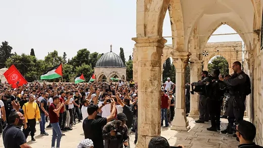 Palestinians protest on the left at the compound that houses Al-Aqsa Mosque and Israeli security stand on the right